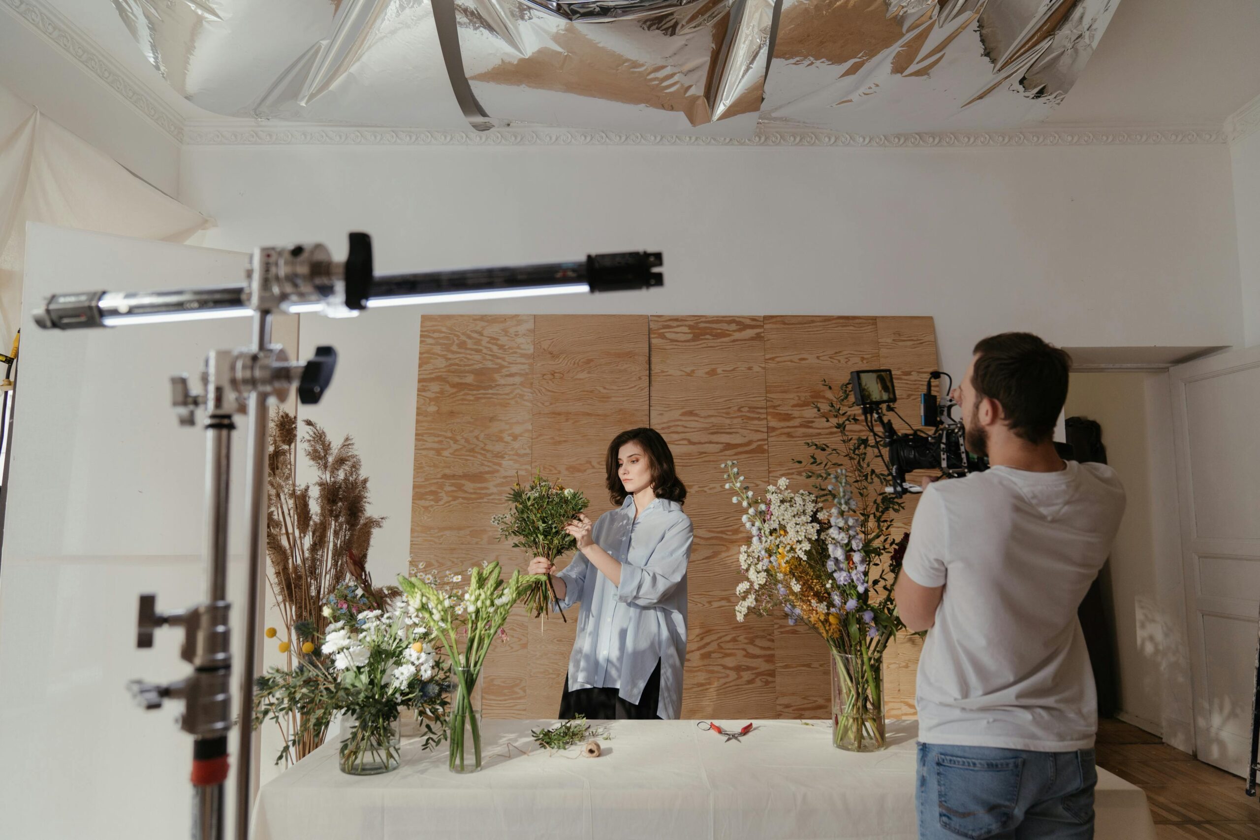 A woman arranges flowers during a photoshoot, captured in a professional studio setting.